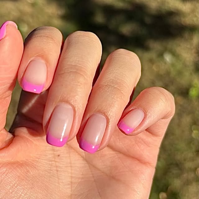 Soft pink nails with bright pink French tips, photographed in natural sunlight.