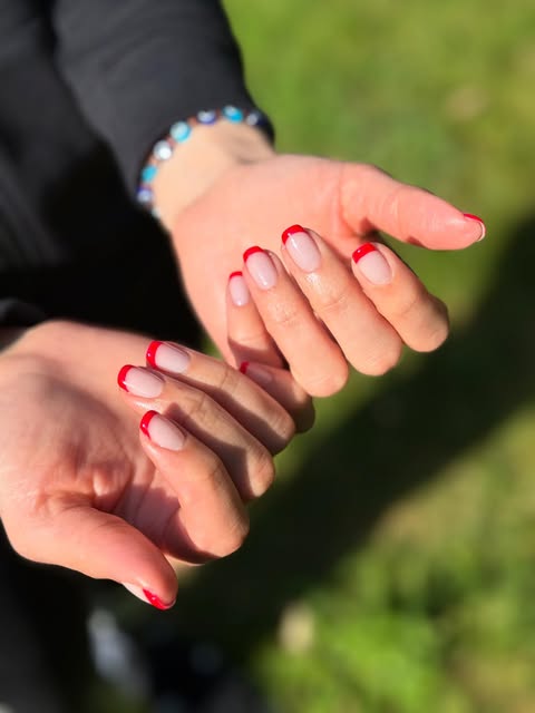 Two hands with sheer pink nails and fine red French tips.